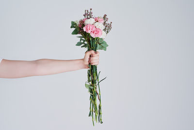 Cropped hand of woman holding bouquet against white background