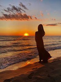 Woman looking at sea against sunset sky