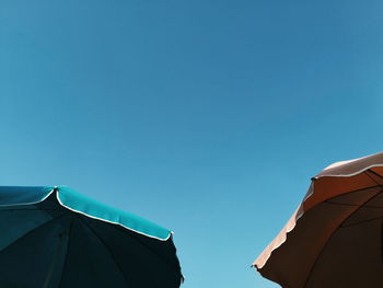 Low angle view of parasols against clear blue sky
