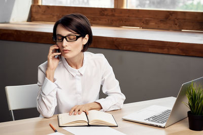 Young woman using mobile phone while sitting on table