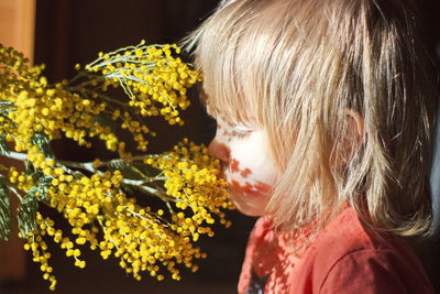 Close-up side view of baby girl smelling yellow flowering plants at home