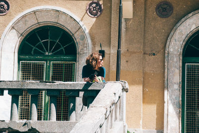 Mature woman standing at building balcony during sunny day