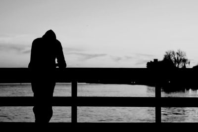 Silhouette man standing by railing against sky