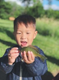 Boy holding dead fish on field