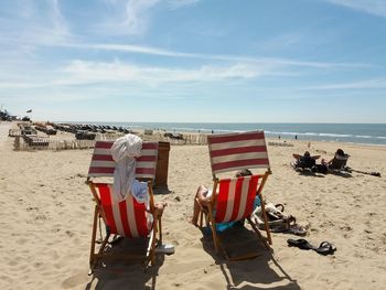 Deck chairs on beach against sky