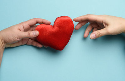 Close-up of hand holding heart shape over blue background