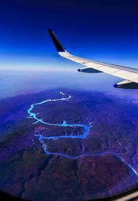 Aerial view of airplane flying over landscape against blue sky