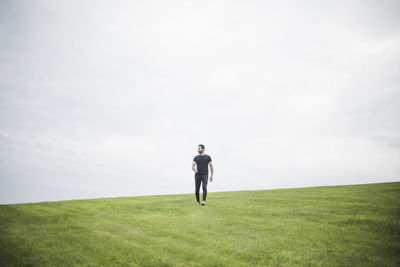 Mid distance view of young man walking on field against cloudy sky