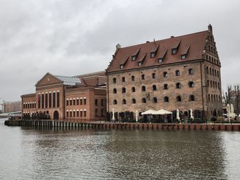 View of buildings by river against cloudy sky