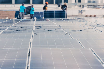 Contemporary solar panels installed in rows in industrial area of factory on background of unrecognizable ethnic workers