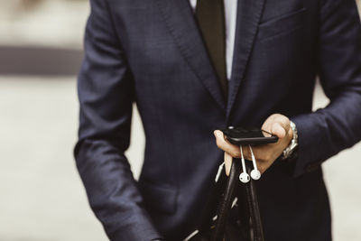 Midsection of male entrepreneur using smart phone while standing outdoors