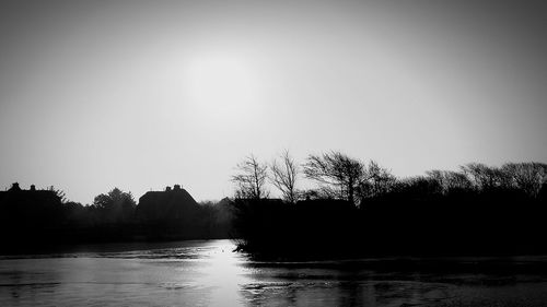 Silhouette trees by lake against clear sky