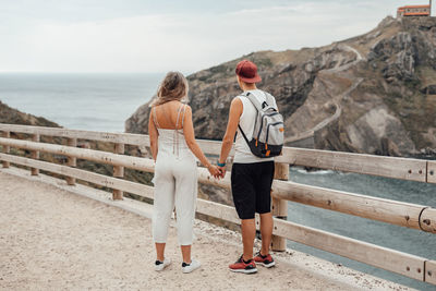 Rear view of couple standing by railing against sky