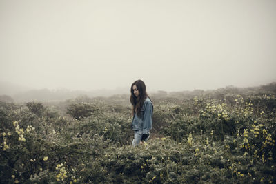 Woman standing amidst flowering plants during foggy weather