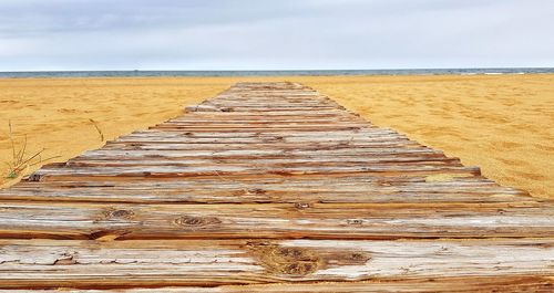 View of wooden walkway leading towards sea against sky