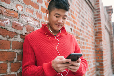 Mid adult man using smart phone while standing against brick wall