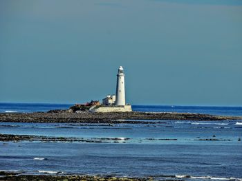 Lighthouse by sea against clear sky