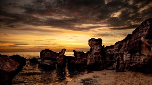 Rocks on beach against sky during sunset