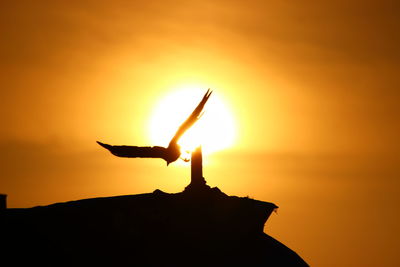 Silhouette person on rock against sky during sunset