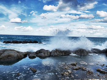 Sea waves splashing on rocks against sky