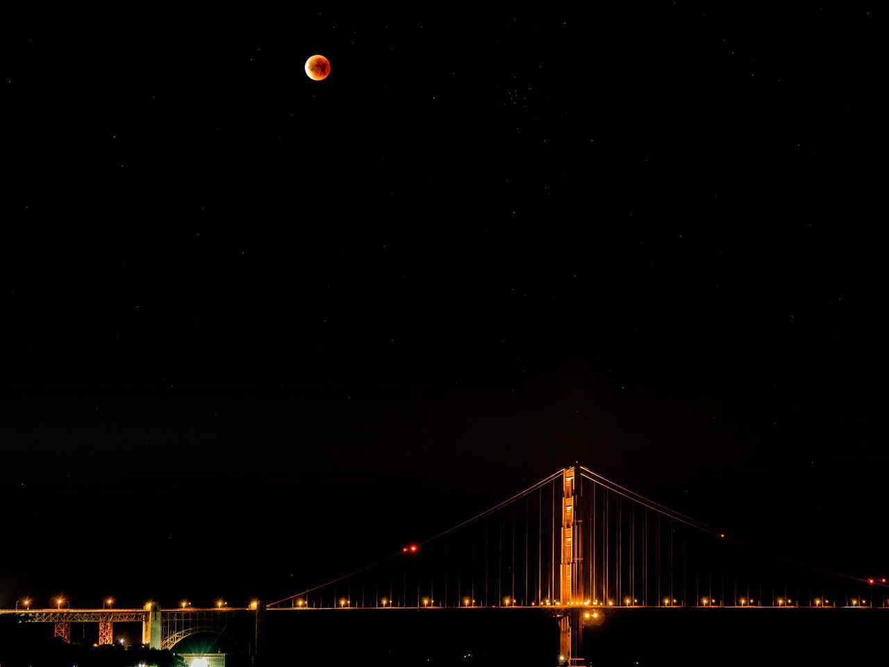 LOW ANGLE VIEW OF ILLUMINATED SUSPENSION BRIDGE AT NIGHT