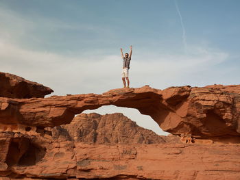 Young guy with hands in the air on rock formation in wadi rum desert