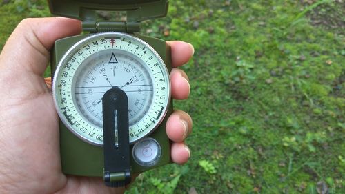 Cropped hand holding navigational compass over field