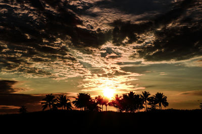 Silhouette trees on landscape against dramatic sky