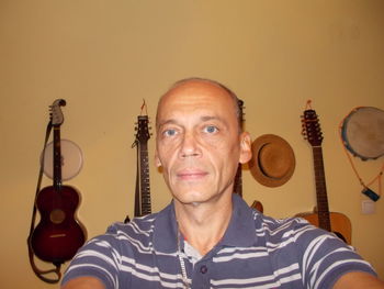 Portrait of mature man against string instruments hanging on wall at home