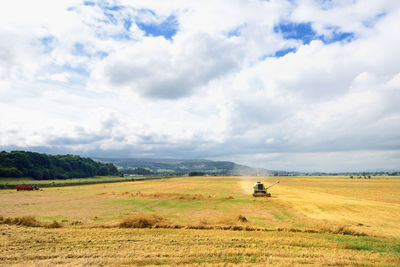 Combine harvester on field against cloudy sky