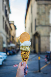 Cropped hand holding ice cream against buildings in city