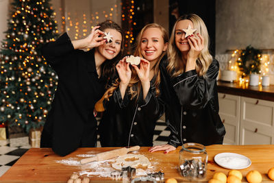 Funny girlfriends laugh and have fun cooking dough cookies at a christmas party in the kitchen