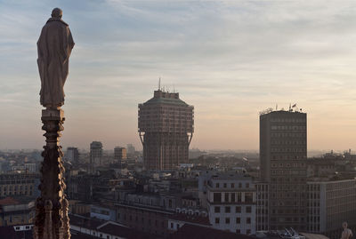 Statue at duomo di milano by buildings in city against sky during sunset