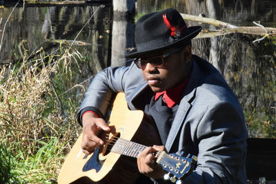 Man wearing suit playing guitar while sitting in yard