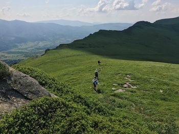 High angle view of people hiking on green mountains during sunny day
