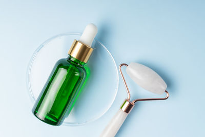 Natural face oil in green pipette bottle and quartz massaging roller on blue background. home spa 