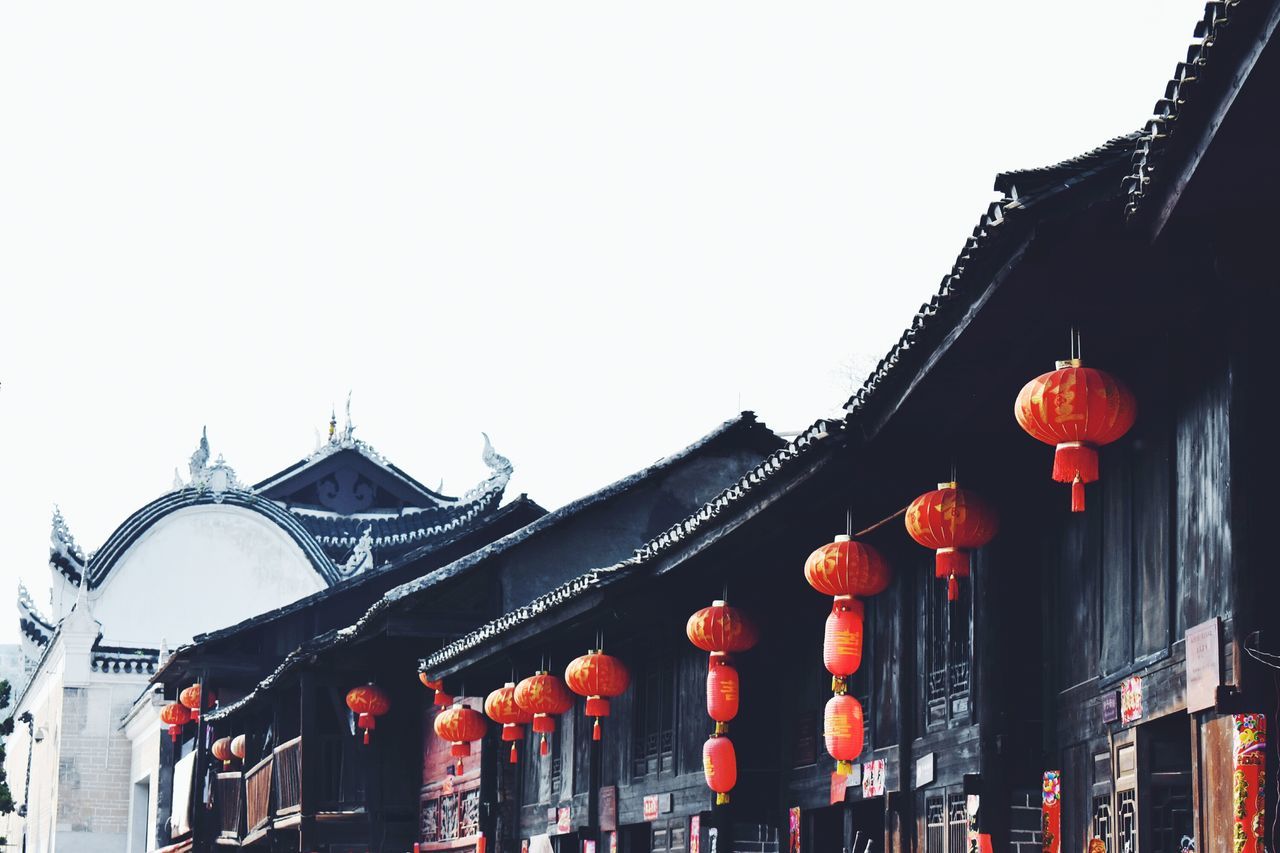 low angle view, architecture, red, built structure, building exterior, clear sky, decoration, hanging, tradition, culture, celebration, illuminated, lighting equipment, cultures, religion, lantern, no people, ornate, outdoors, copy space