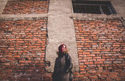 Low angle view of woman standing against brick wall