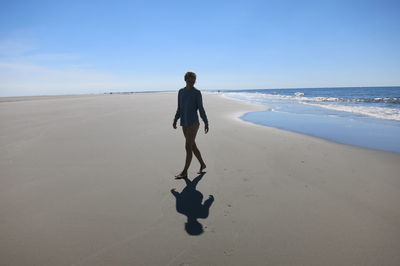 Full length of man walking on beach against clear sky