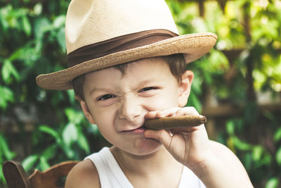 Portrait of cute boy wearing hat while holding cigar outdoors