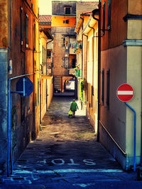 Rear view of woman walking in alley amidst buildings