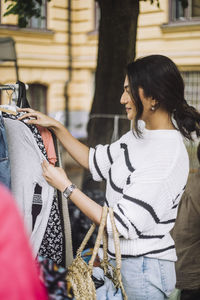 Side view of woman choosing dress from rack while shopping at flea market