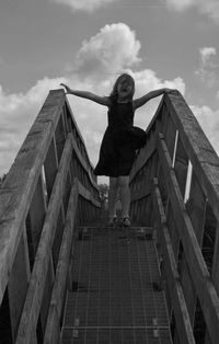 Low angle view of girl standing on footbridge against sky