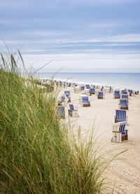 Hooded chairs on beach against sky