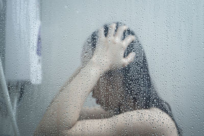 Close-up of wet woman bathing seen through glass