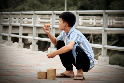 Side view of young man looking away while sitting on wood