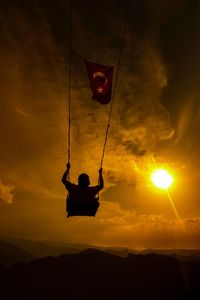 Low angle view silhouette of person sitting on swing against sky during sunset