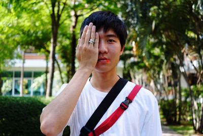 Portrait of young man with flower in mouth while covering eye