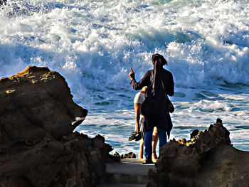 People standing on rock by sea against sky