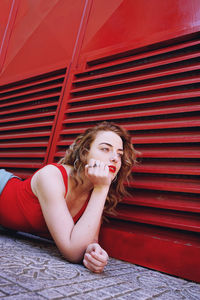 Low angle view of young woman leaning on footpath by red shutter